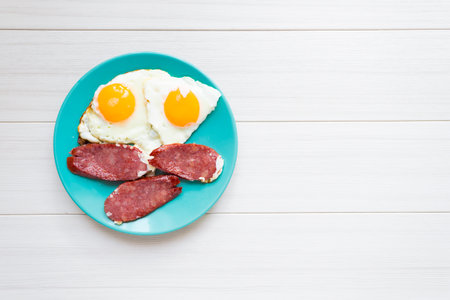 Breakfast of fried smoked sausage and eggs on a blue plate.の写真素材
