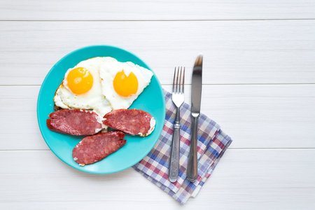 Breakfast of fried smoked sausage and eggs on a blue plate.の写真素材