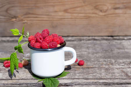 White mug with red raspberries on an old wooden table. Soft focusの写真素材