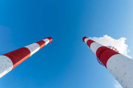 Large red, white brick pipes of a factory on a blue sky background blowing smoke into the atmosphere on a sunny bright day. Bottom viewの写真素材