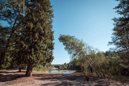 A bright summer sunny day. The blue sky and trees are reflected on the surface of the river. On the river bank there is a green trees.の写真素材