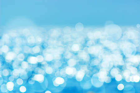 Soft focus bokeh light effects over a rippled, blue water background with lens flare.の写真素材