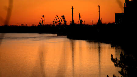 Sunset on the Volga river. Silhouettes of port cranes on the river bank. Views Of the river port of Bor. April 2022.の写真素材