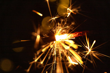 Glittering burning sparkler against blurred bokeh light background