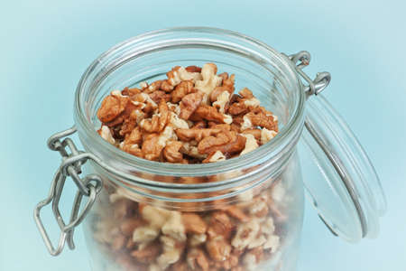 Peeled walnuts in a glass jar. On a blue background.