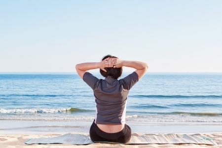 The girl is sitting on the beach practicing yoga. In summer the sea.の写真素材