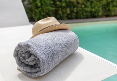 Straw hat on the sun lounger and a towel by the pool. Vacation with a tourist.の写真素材