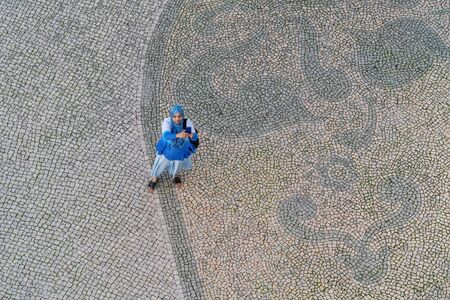 Faro Portugal, December 12, 2019 - Muslim girl on the square in the old town, taking selfies. Top view, on the background of a cobblestone pattern.のeditorial素材