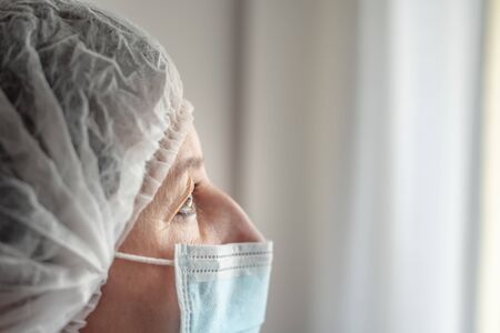Tired nurse doctor in protective mask and cap against coronavirus type Covid 19. Close-up.