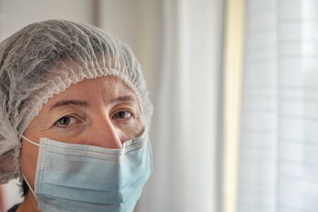 Tired nurse doctor in protective mask and cap against coronavirus type Covid 19.