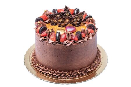 Chocolate cake decorated with cream, strawberries, cookies on a golden plate, a tray. Close-up.