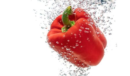 Juicy red ecological, pepper falling into clean water creates bubbles. Isolated on a white background.の写真素材