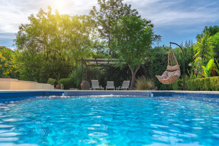 Luxurious pool in the garden of a private villa, hanging chair with pillows for leisure tourists, in summer. Portugal, Algarveの写真素材