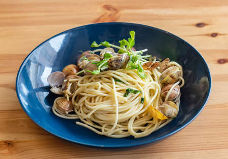 Blue bowl of spaghetti with clams that is placed on a wooden table. Seafood simplicity. High quality photoの写真素材