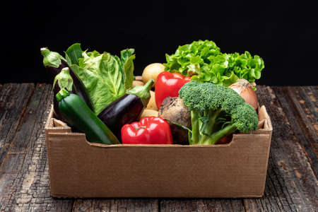 Colorful vegetable basket and filled with broccoli, lettuce, aubergines, onions, zucchini, peppers and potatoes. On a wooden background, close-upの写真素材