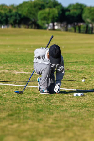 Golfer boy crouching down and placing a ball on a tee support, on a grass course. Preparing his next shot. High quality photoの写真素材