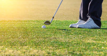 Zoomed in shot of a ball that is placed on a golf course and a golfer that is about to swing. High quality photoの写真素材