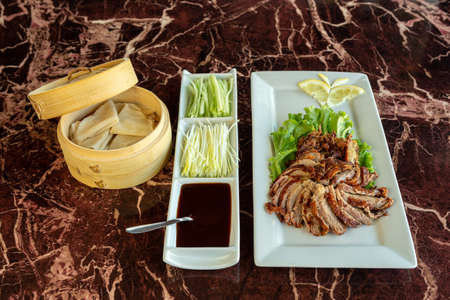 Chinese peking duck decorated with some lemon and lettuce besides some soy sauce and sprouts on a marbled surface.の写真素材