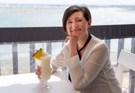 A middle-aged woman, in a bar, drinks a fruit coconut cocktail, with a slice of pineapple. Resting...