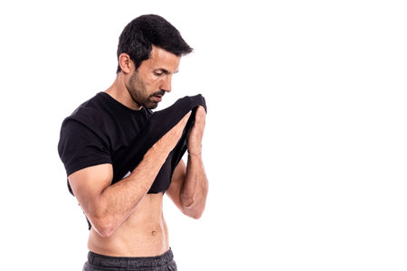 A young European man, an athlete, wipes sweat from his forehead with a T-shirt. After a hard workout. Stress and fatigue. On a white background. High quality photoの写真素材