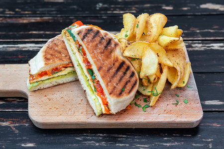 Grilled veggie sandwich with vegetables and herbs, cut in half on a wooden kitchen board. Garnish with potatoes. Close-up. High quality photoの写真素材