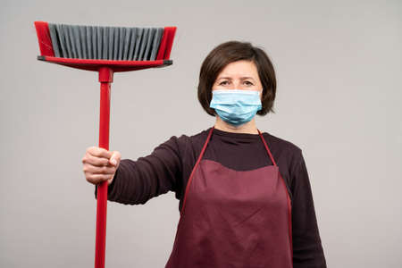 A woman in a surgical mask, a middle-aged European, a cleaner, holds a mop in her hands. The concept of cleaning . High quality photoの写真素材