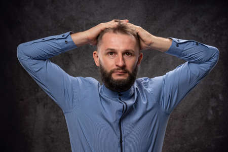 Emotionally shocked young man, holding his head with his hands, surprised and frightened. On a dark...