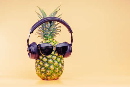 Creative idea of a pineapple image of a person wearing headphones and glasses as a relaxing tourist on vacation or listening to podcasts. On a yellow background. High quality photoの写真素材