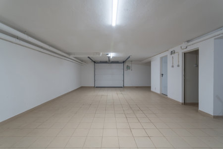 This garage features ample space with clean, tiled floors and bright lighting. Ideal for parking vehicles or storing belongings in a residential areaの写真素材