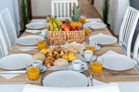 A beautifully arranged breakfast table features fresh fruits, various pastries, and beverages in a bright, modern dining spaceの写真素材