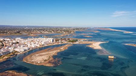 Aerial view of Fuzeta town along Ria Formosa lagoon system with white buildings, sandbanks and clear turquoise water under blue sky in Algarve, Portugal. Concept of natural coastal tourismの写真素材