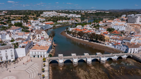 Aerial view of Tavira with historic Roman bridge over the Gilao River, traditional buildings and green hills in background under blue sky in Algarve, Portugal. Concept of cultural heritage tourismの写真素材