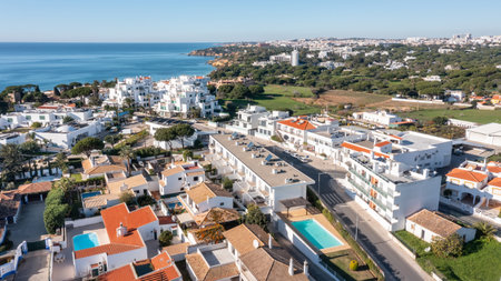 Aerial view of Olhos de Agua in Albufeira with white coastal houses, swimming pools and Atlantic Ocean under clear blue sky in Algarve, Portugal. Concept of relaxed seaside living and tourismの写真素材