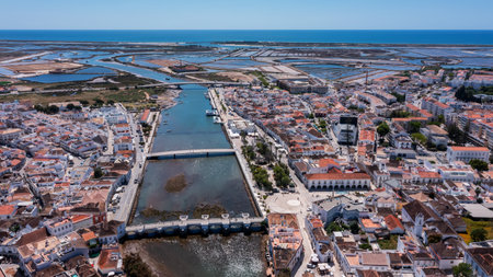 Aerial view of Tavira with Roman bridge over Gilao River traditional whitewashed buildings salt pans and Atlantic Ocean in the distance under clear sky in Algarve. Concept of historical coastal charmの写真素材