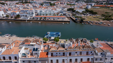 Aerial view of Tavira town with traditional tiled rooftops and boats along the Gilao River under bright sunlight in Algarve, Portugal. Concept of historic riverside tourismの写真素材