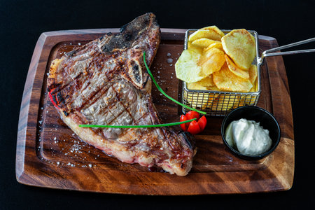 Grilled steak served on a wooden platter with crispy potato chips and fresh herbs, showcasing a delicious culinary presentationの写真素材