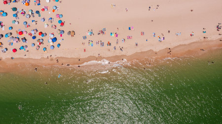 Aerial view of vibrant beach scene with colorful umbrellas and sunbathers enjoying sunny day by the ocean, capturing summer leisure atmosphere. Tavira Portugal Algarveの写真素材