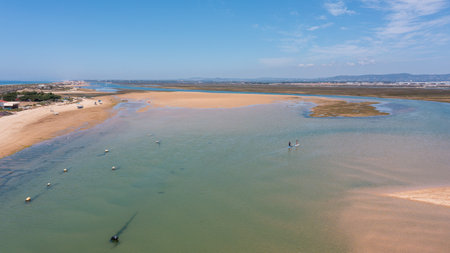 Drone captures Ria Formosa and Praia de Faro showing calm waters, sandy areas, and people engaging with nature in Faro, Portugal on a sunny dayの写真素材
