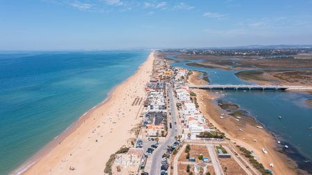 Aerial view shows Praia de Faro with its long sandy beach and the nearby Ria Formosa. People enjoy the beach while boats rest in the waterの写真素材
