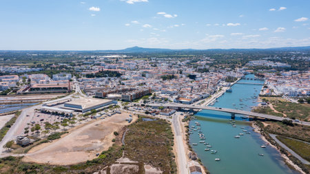 Tavira in Algarve Portugal with buildings along the Gilao river and green areas. This is a sunny day with boats in the water and hills in the backgroundの写真素材