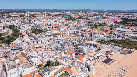 People relax at Praia dos Pescadores while families walk along the beach. The marina is busy with boats and the town of Albufeira is vibrantの写真素材