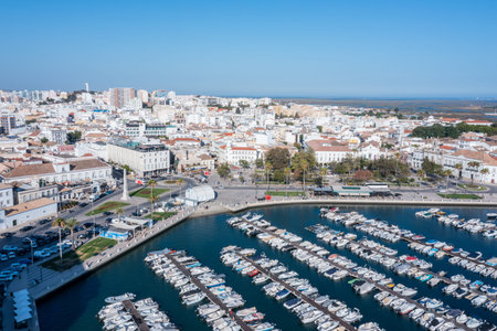 Visitors enjoy the marina view in Faro, Algarve, with boats docked and the old town visible under...