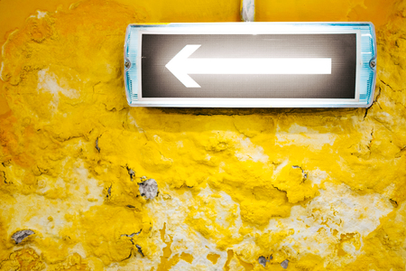 An arrow with a backlight on the yellow wall with destroyed texture.