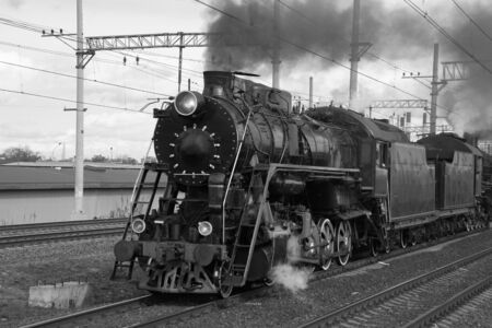 Black and white retro steam train in clouds of smoke rides by rail, rolling touristsの写真素材