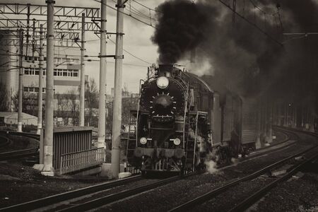 Black and white retro steam train in clouds of smoke rides by rail, rolling touristsの写真素材