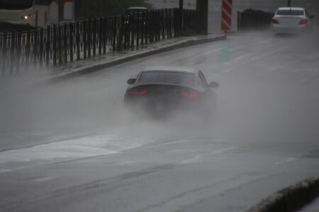 cars drive in heavy rain along the road, spraying fountains of water from puddles in all directions