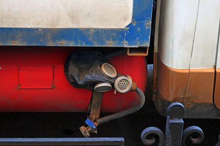 old rubber gas mask on a red gas cylinder under the car body