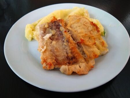 fried fish with golden brown crust and mashed potatoes on a white plateの写真素材