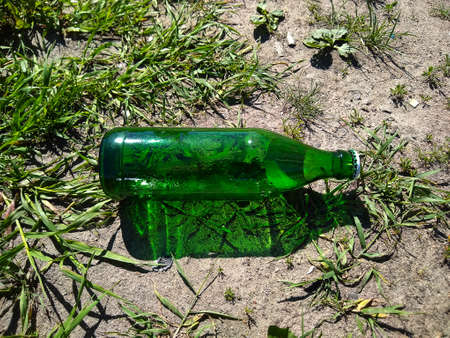 An empty green bottle, closed by crown plug, lying on the ground among green grassの写真素材
