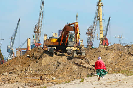 excavator on a large pile of sand and construction machinery in the distance at a construction site,...